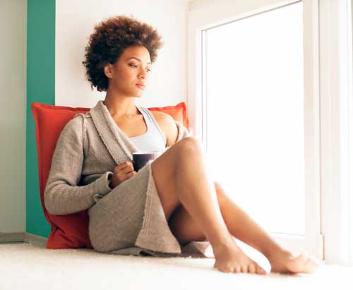 Young-woman-with-coffee-cup-sitting-against-a-red-pillow-looking-out-window