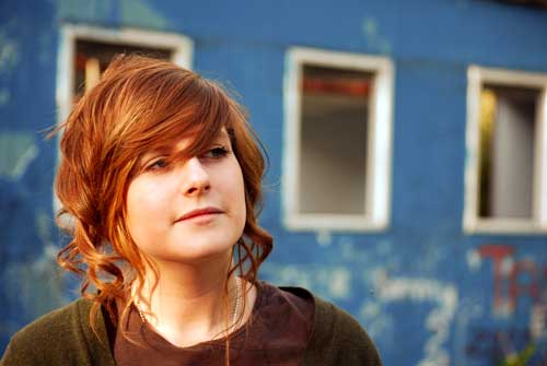 Young-woman-with-red-hair-standing-in-front-of-blue-wall-with-windows